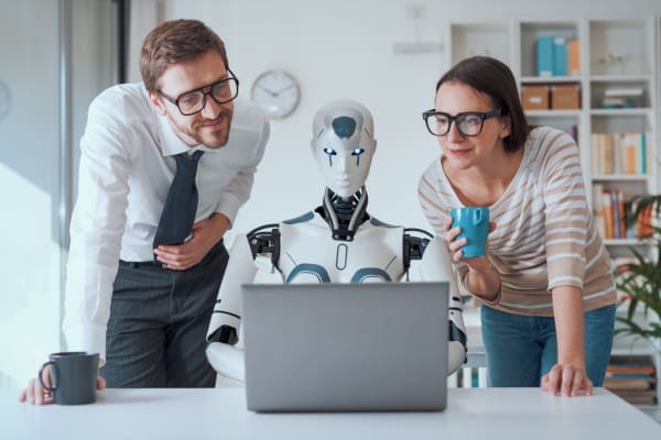 Two people at a desk with a robot looking at a laptop screen